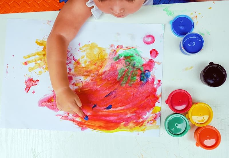 A child pressing colorful handprints onto paper beside open pots of paint